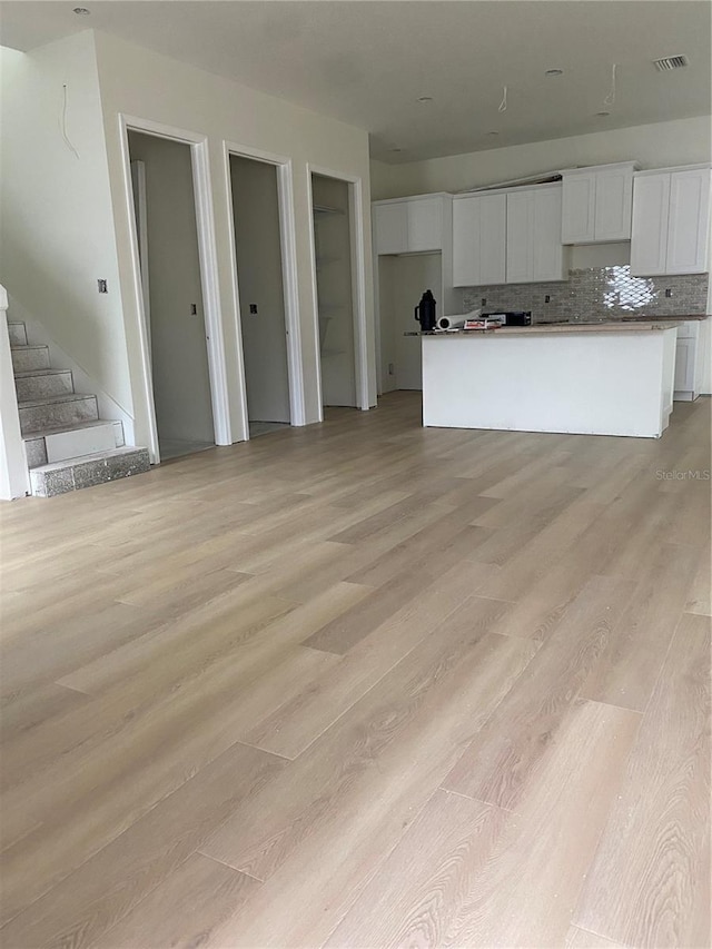 kitchen featuring decorative backsplash, light hardwood / wood-style flooring, white cabinets, and a kitchen island with sink