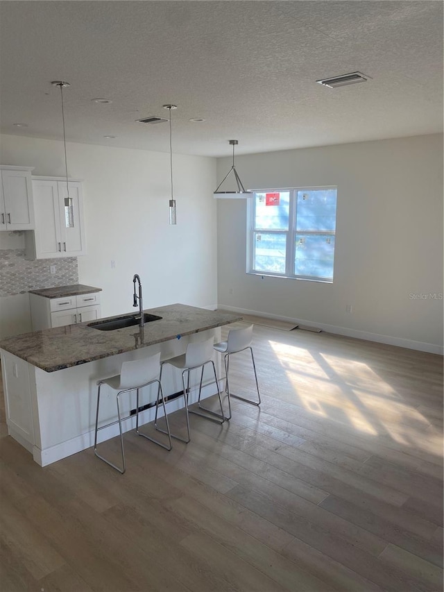 kitchen with decorative light fixtures, tasteful backsplash, white cabinetry, sink, and a kitchen bar