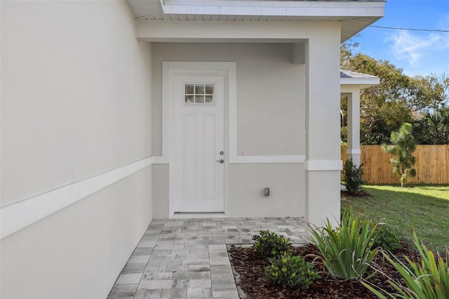 view of exterior entry featuring a yard, fence, and stucco siding