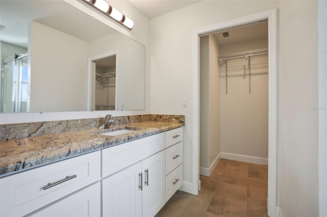 full bath with a walk in closet, vanity, and baseboards