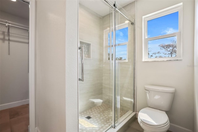 full bathroom featuring a stall shower, baseboards, a spacious closet, and toilet