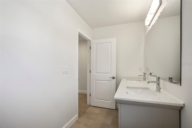 bathroom featuring a textured ceiling, double vanity, a sink, and baseboards