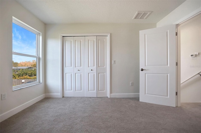 unfurnished bedroom featuring carpet, a closet, visible vents, a textured ceiling, and baseboards