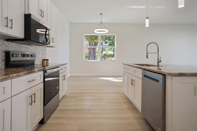 kitchen featuring stainless steel appliances, backsplash, a sink, light stone countertops, and light wood-type flooring