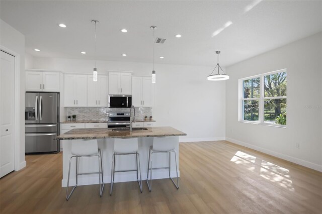 kitchen with stainless steel appliances, decorative backsplash, a kitchen island with sink, a sink, and a kitchen breakfast bar