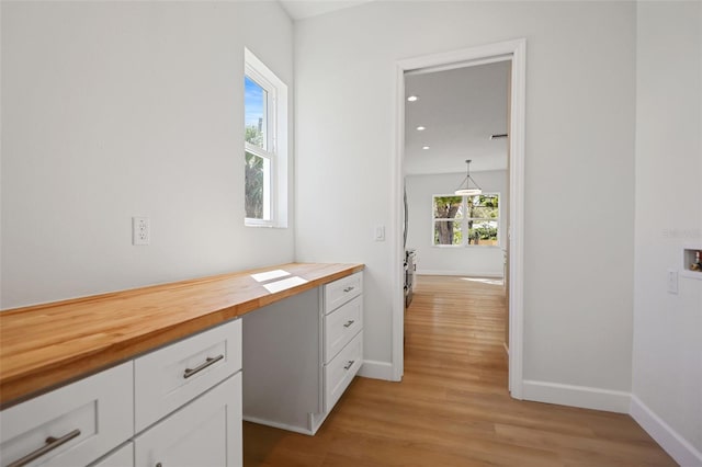 interior space featuring butcher block counters, white cabinetry, light wood-style flooring, and baseboards