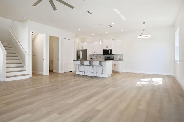 kitchen featuring tasteful backsplash, a breakfast bar, open floor plan, stainless steel appliances, and white cabinetry