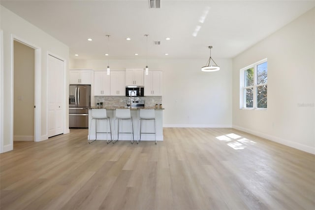 kitchen featuring a center island with sink, a kitchen breakfast bar, stainless steel appliances, white cabinetry, and backsplash