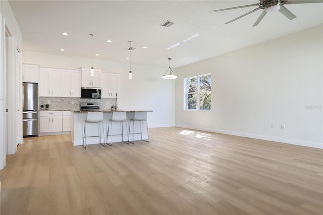 kitchen featuring stainless steel appliances, a breakfast bar, visible vents, open floor plan, and backsplash