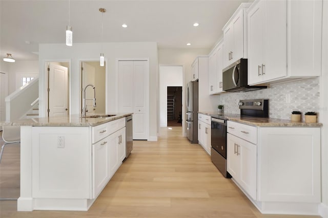 kitchen featuring stainless steel appliances, backsplash, white cabinetry, a sink, and an island with sink