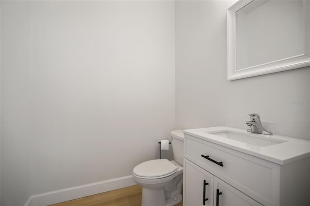 half bath featuring toilet, baseboards, wood finished floors, and vanity