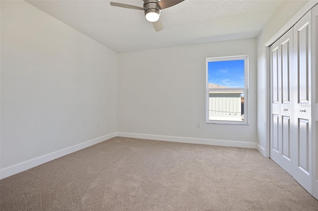 unfurnished bedroom featuring ceiling fan, a textured ceiling, light colored carpet, baseboards, and a closet