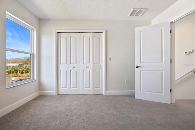 unfurnished bedroom featuring a closet, visible vents, carpet flooring, a textured ceiling, and baseboards