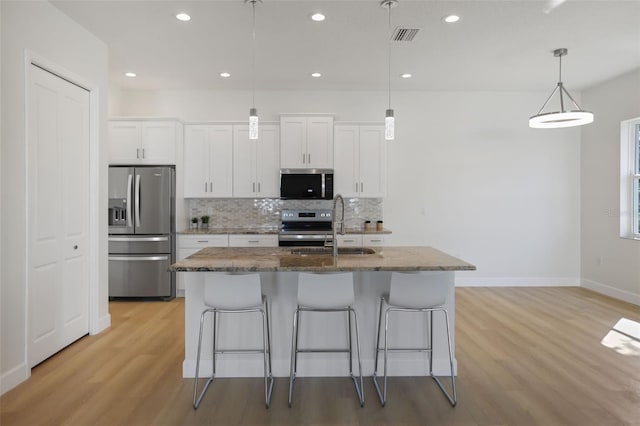 kitchen with a center island with sink, decorative backsplash, appliances with stainless steel finishes, a sink, and a kitchen bar