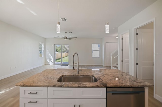 kitchen featuring hanging light fixtures, stainless steel dishwasher, open floor plan, white cabinets, and a sink