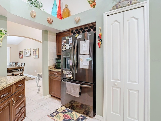 kitchen featuring stainless steel fridge, light tile patterned floors, light stone countertops, and vaulted ceiling