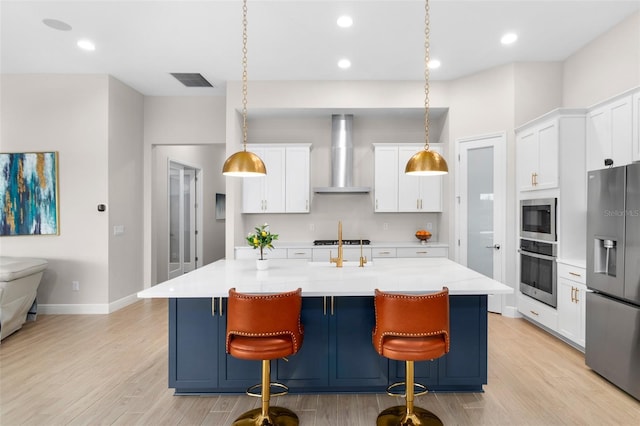 kitchen with appliances with stainless steel finishes, a center island with sink, hanging light fixtures, and wall chimney exhaust hood