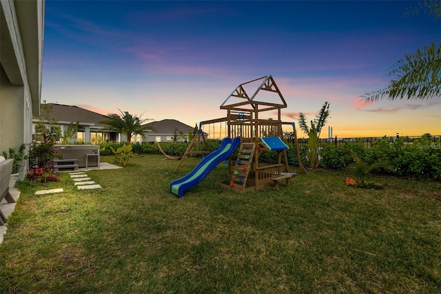 playground at dusk featuring a yard and a hot tub