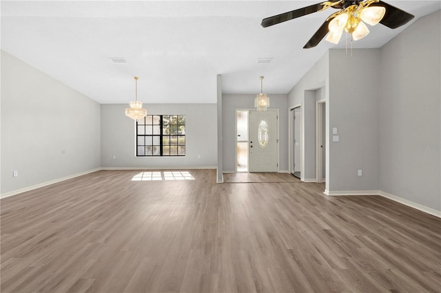 unfurnished living room featuring ceiling fan with notable chandelier, wood-type flooring, and vaulted ceiling