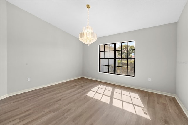 empty room with wood-type flooring and an inviting chandelier