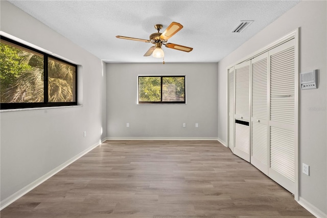 unfurnished bedroom featuring ceiling fan, a closet, a textured ceiling, and light wood-type flooring