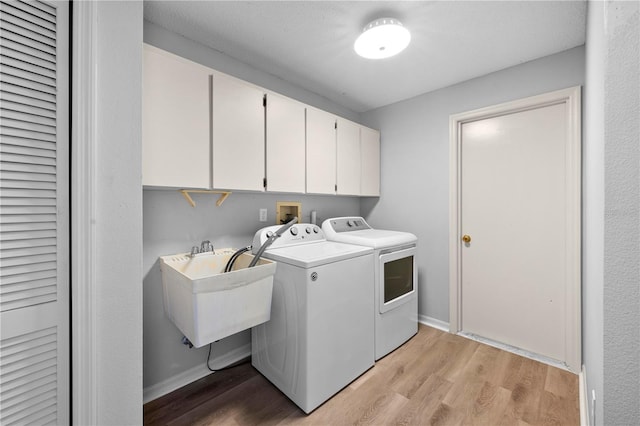 clothes washing area featuring washing machine and clothes dryer, sink, cabinets, and light hardwood / wood-style floors