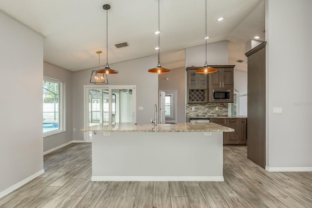 kitchen with tasteful backsplash, a kitchen island with sink, decorative light fixtures, light stone counters, and sink