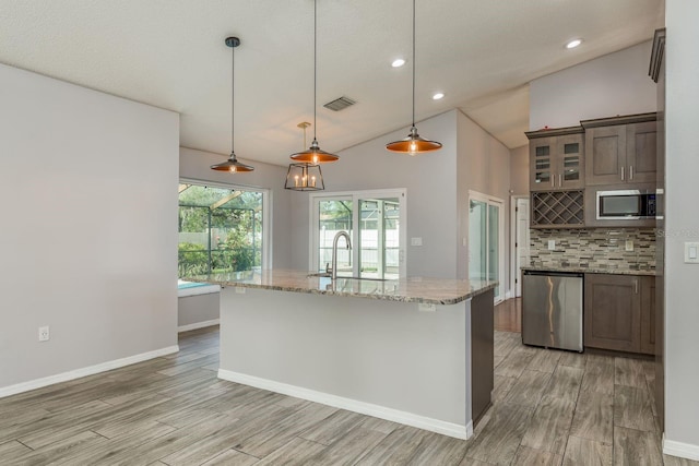 kitchen featuring a center island with sink, appliances with stainless steel finishes, decorative light fixtures, light stone counters, and sink