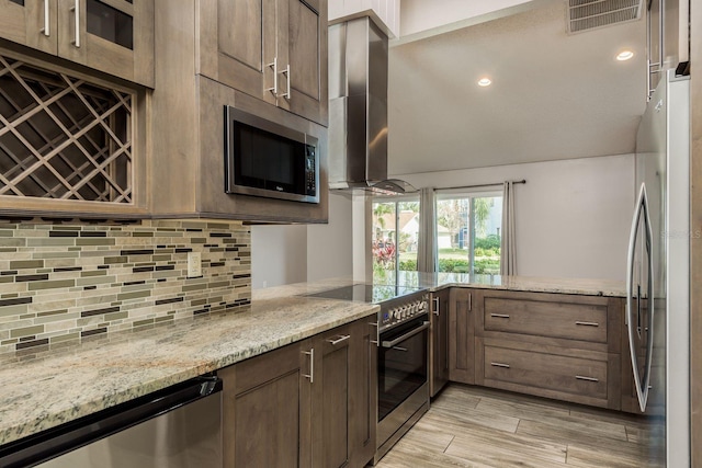 kitchen featuring tasteful backsplash, kitchen peninsula, stainless steel appliances, ventilation hood, and light stone counters