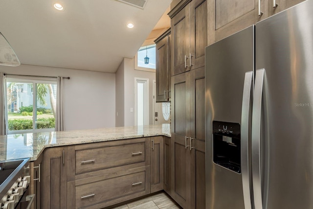 kitchen featuring stainless steel fridge with ice dispenser, kitchen peninsula, light stone counters, and stove