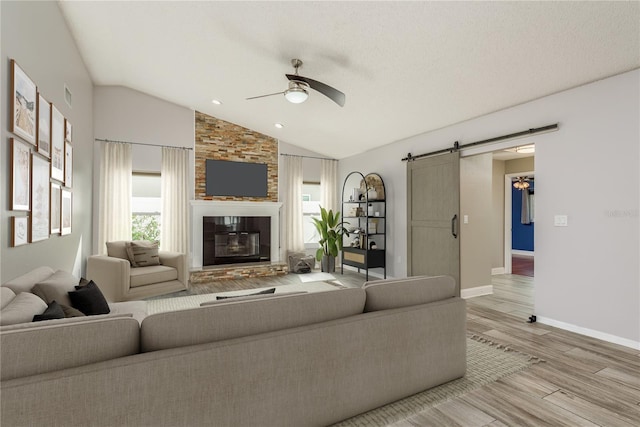 living room with light hardwood / wood-style floors, a barn door, ceiling fan, lofted ceiling, and a fireplace