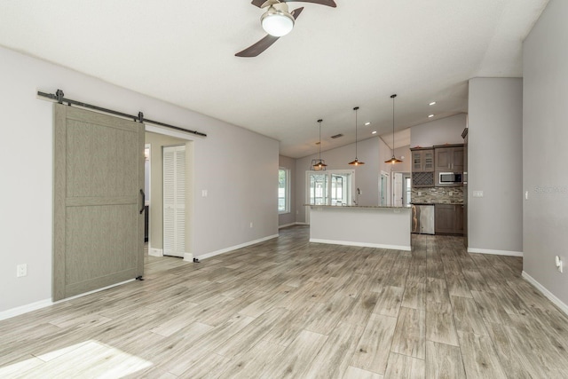 unfurnished living room with ceiling fan, a barn door, lofted ceiling, and light hardwood / wood-style flooring