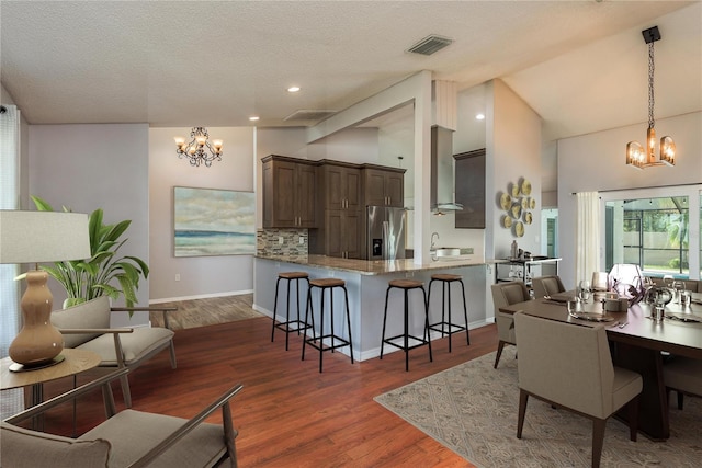 kitchen with stainless steel fridge with ice dispenser, kitchen peninsula, dark hardwood / wood-style flooring, dark brown cabinets, and pendant lighting