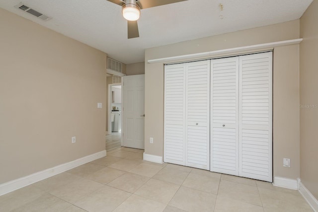 unfurnished bedroom featuring ceiling fan, a closet, light tile patterned flooring, and washer / dryer