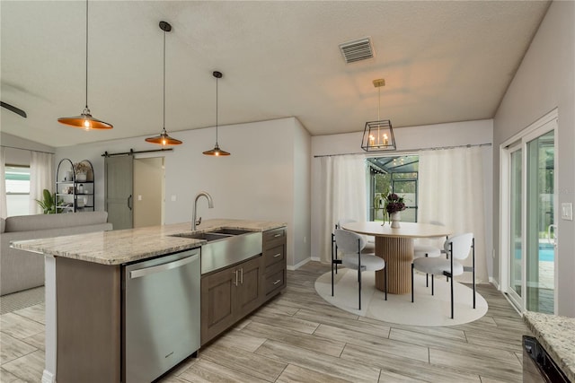 kitchen featuring decorative light fixtures, a barn door, stainless steel dishwasher, sink, and a kitchen island with sink