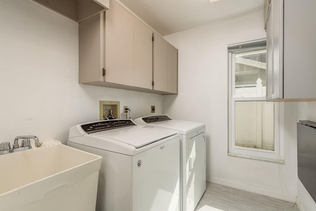 clothes washing area with cabinets, sink, a textured ceiling, and washing machine and dryer