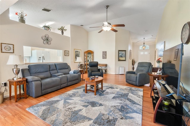 living room with a textured ceiling, light hardwood / wood-style flooring, high vaulted ceiling, and ceiling fan