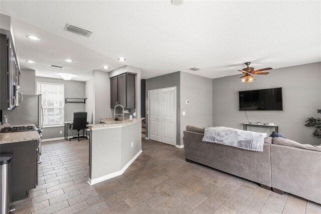 kitchen featuring a textured ceiling, ceiling fan, light stone counters, and a kitchen island with sink