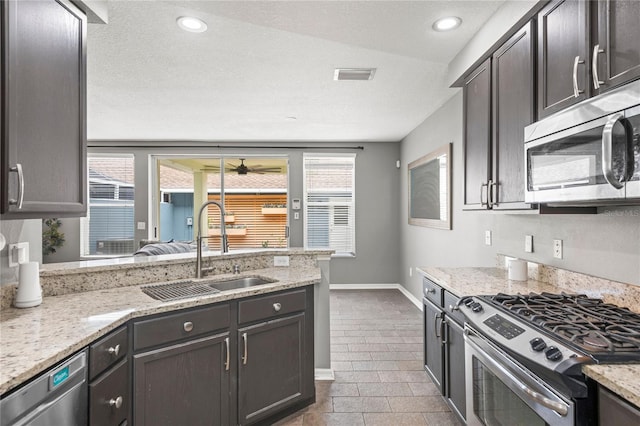 kitchen with light stone countertops, appliances with stainless steel finishes, dark brown cabinetry, vaulted ceiling, and sink