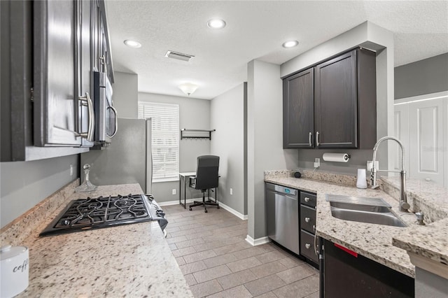 kitchen with light stone counters, dark brown cabinetry, sink, and stainless steel appliances