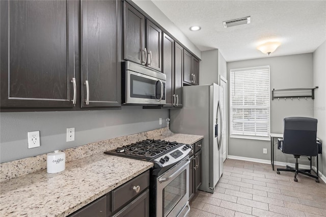 kitchen featuring dark brown cabinetry, light stone counters, a textured ceiling, and appliances with stainless steel finishes