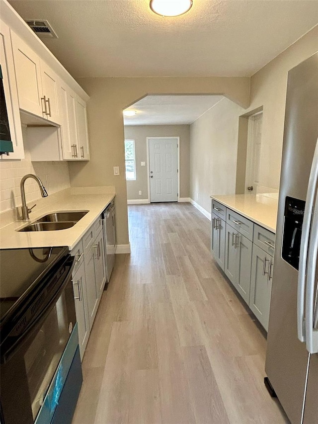 kitchen featuring a textured ceiling, stainless steel appliances, sink, light hardwood / wood-style flooring, and white cabinetry