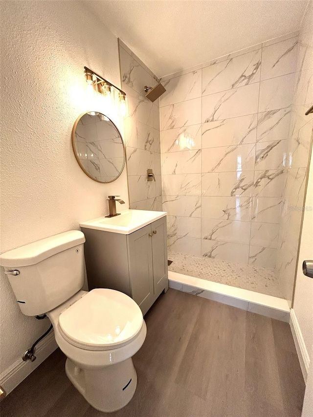 bathroom with a tile shower, hardwood / wood-style flooring, vanity, and toilet