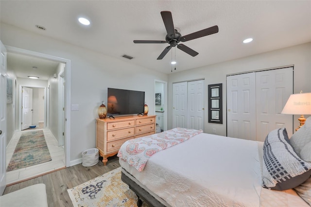 bedroom with two closets, light hardwood / wood-style floors, and ceiling fan