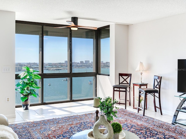 tiled living room featuring ceiling fan, a textured ceiling, and a wall of windows