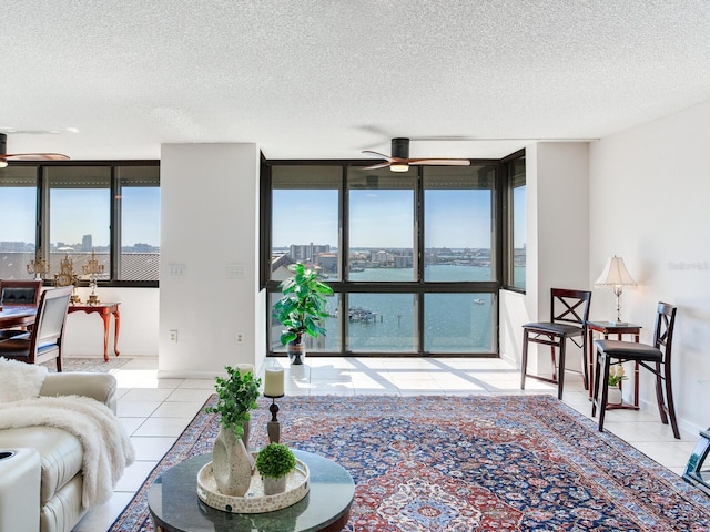 tiled living room featuring ceiling fan, a wall of windows, and a textured ceiling