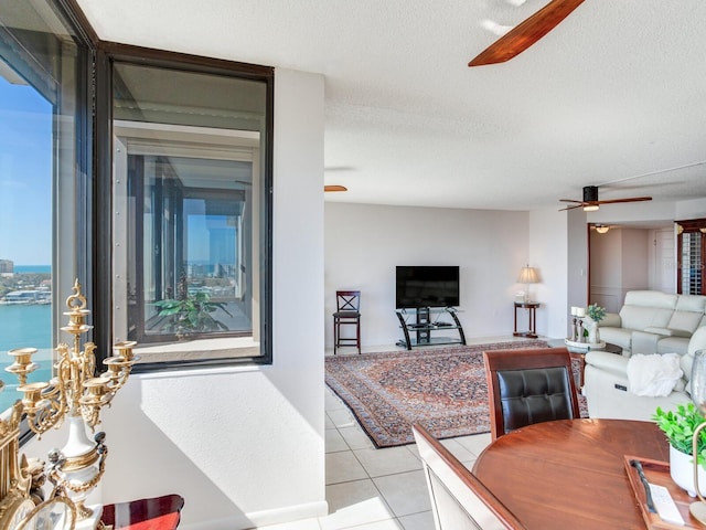 tiled living room featuring a wealth of natural light, a water view, a textured ceiling, and ceiling fan