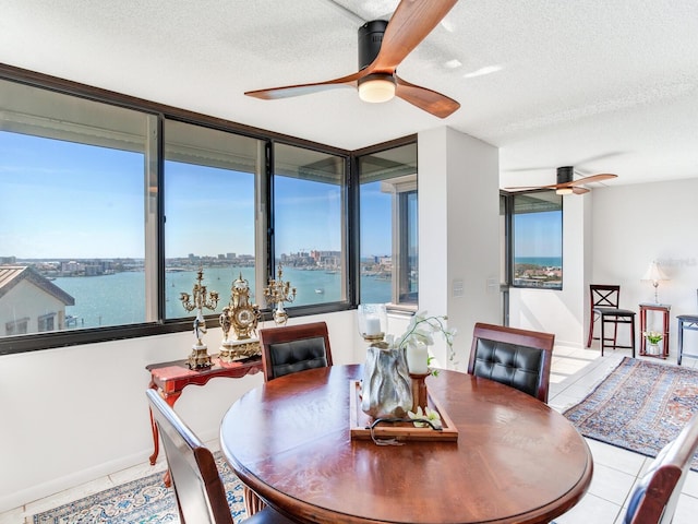 tiled dining room with ceiling fan, a water view, and a textured ceiling