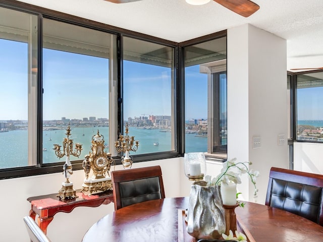 dining space featuring ceiling fan, a water view, and a textured ceiling