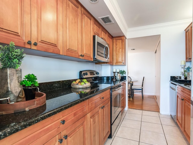 kitchen with dark stone countertops, crown molding, light tile patterned floors, and appliances with stainless steel finishes